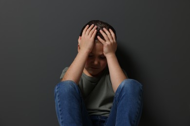 Photo of Child abuse. Upset girl sitting on floor near grey wall