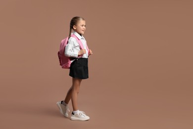 Photo of Happy schoolgirl with backpack on brown background, space for text