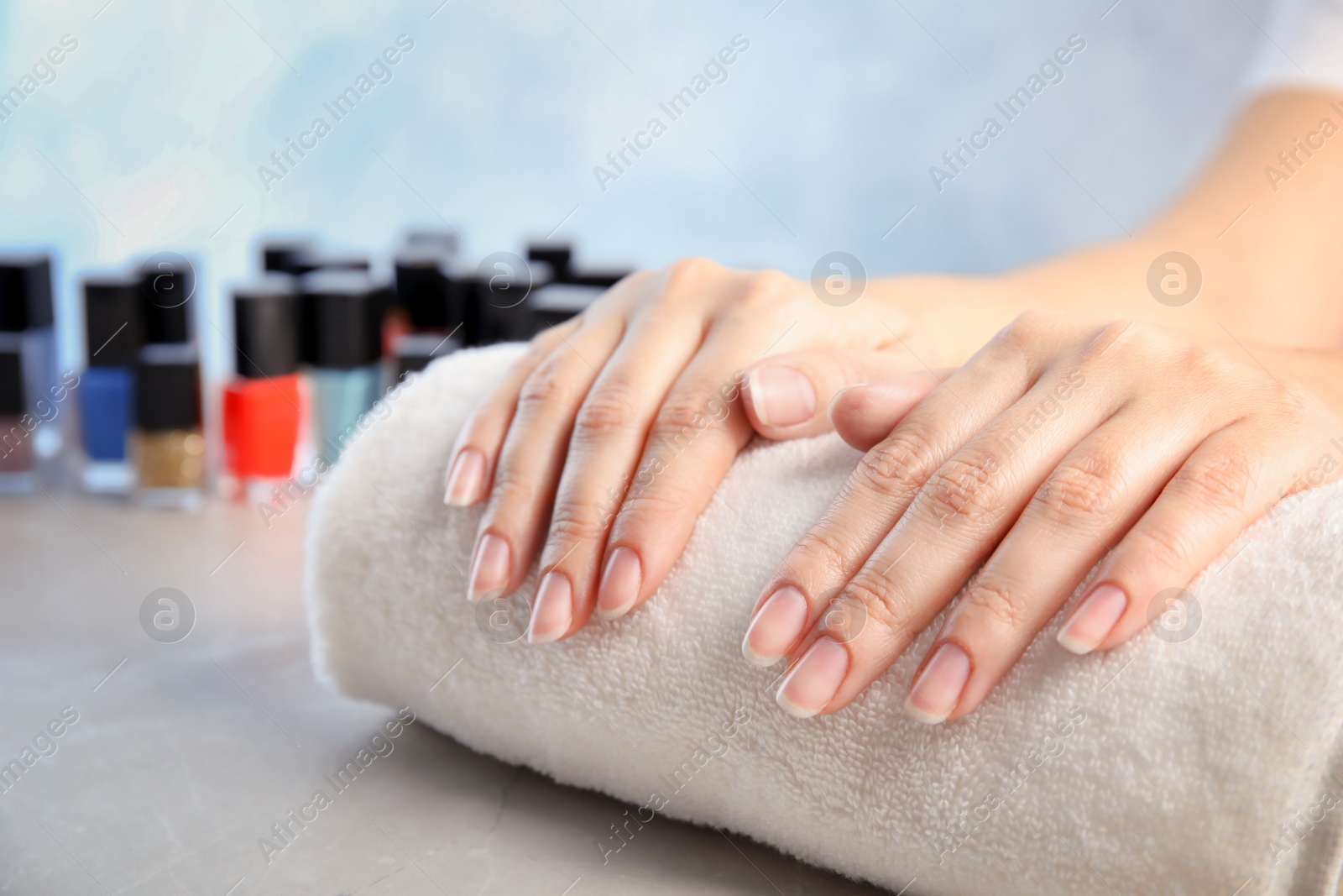 Photo of Young woman waiting for manicure near bottles of nail polish at table in salon, closeup. Space for text