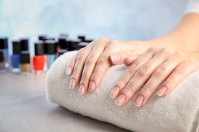 Photo of Young woman waiting for manicure near bottles of nail polish at table in salon, closeup. Space for text