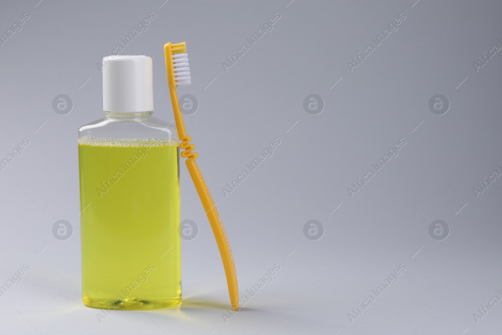 Photo of Fresh mouthwash in bottle and toothbrush on grey background. Space for text