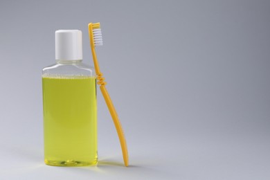 Photo of Fresh mouthwash in bottle and toothbrush on grey background. Space for text