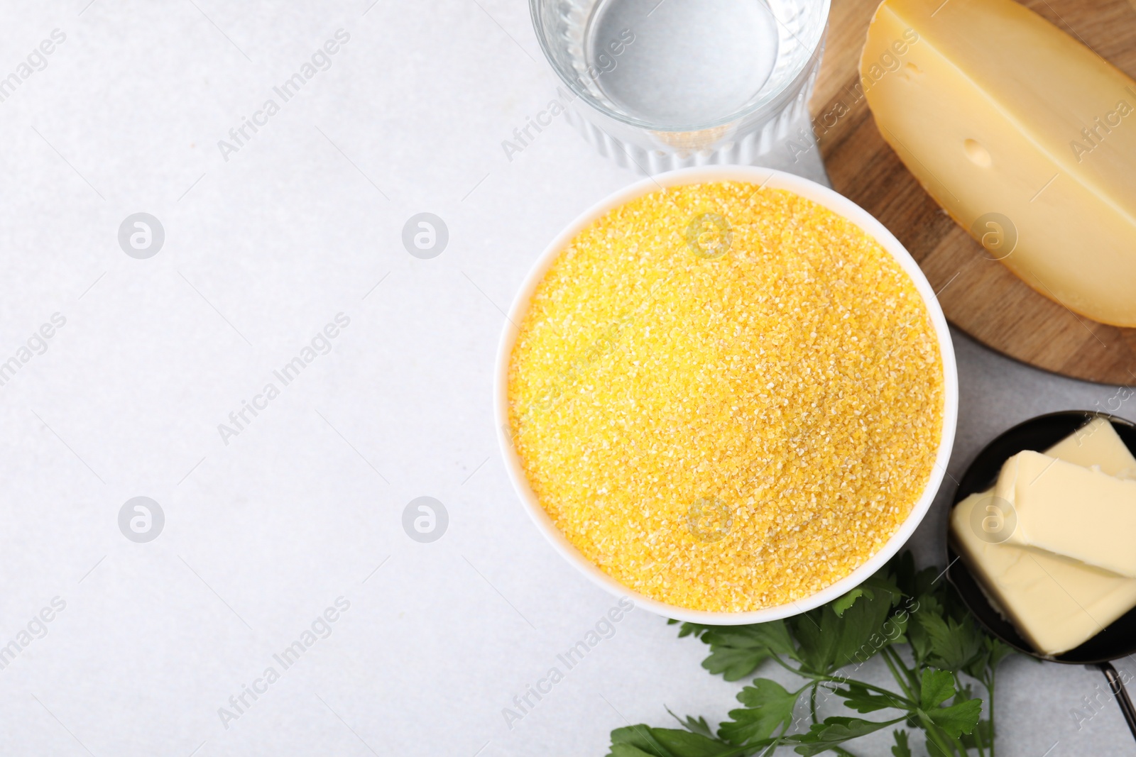 Photo of Raw cornmeal in bowl, water, cheese, parsley and butter on light table, flat lay. Space for text