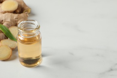 Glass bottle of essential oil and ginger root on white table, space for text