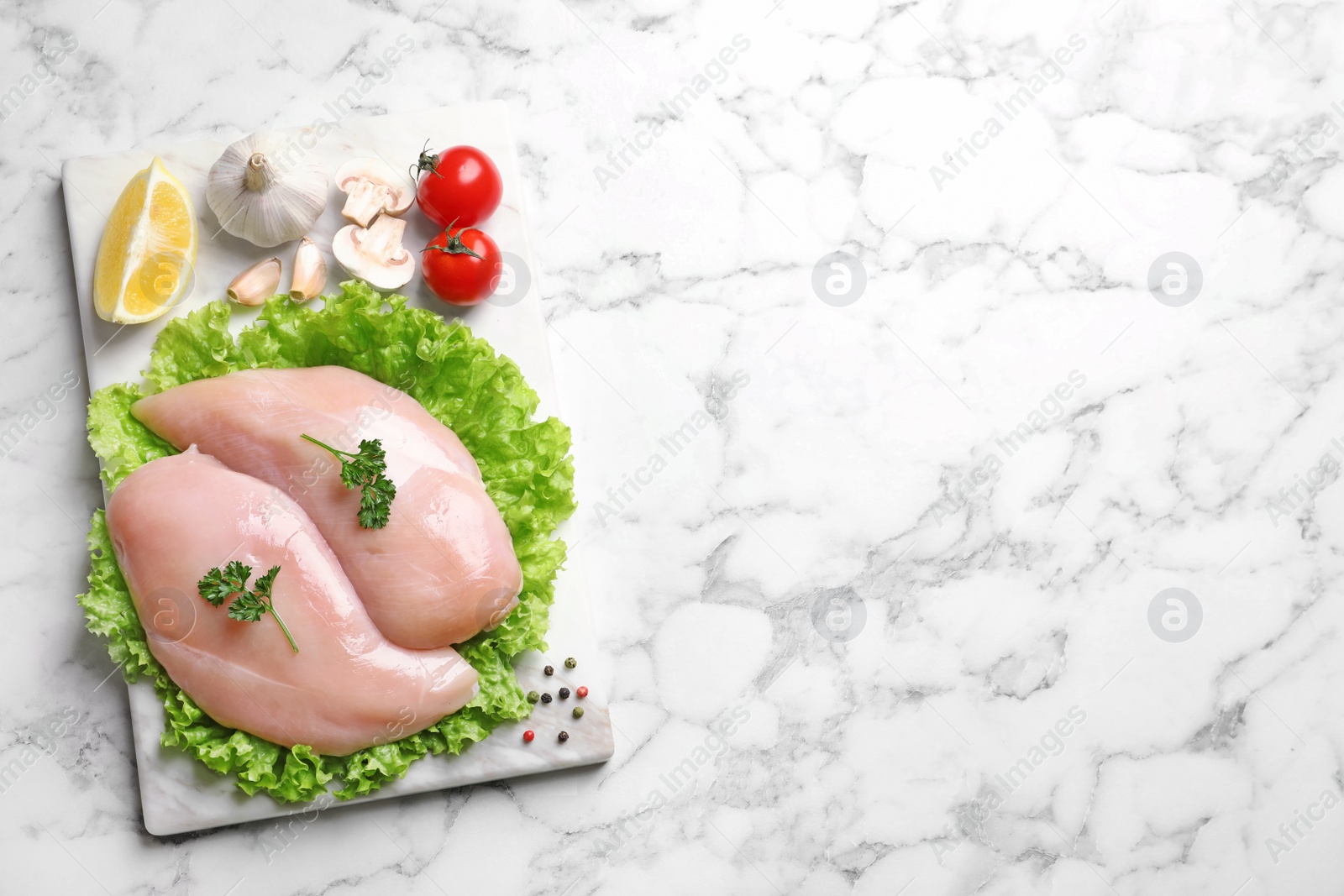 Photo of Board with raw chicken breasts and ingredients on marble background, top view. Space for text