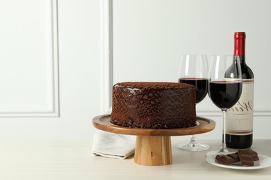 Photo of Delicious truffle cake, chocolate pieces and red wine on light wooden table, space for text
