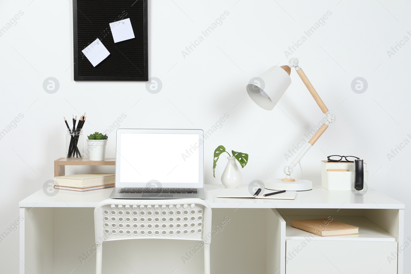 Photo of Cozy workspace with laptop, lamp and stationery on wooden desk at home