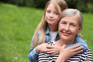 Portrait of happy grandmother hugging her granddaughter outdoors, space for text