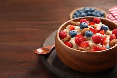 Photo of Tasty oatmeal porridge with berries and almond nuts in bowl served on wooden table, space for text