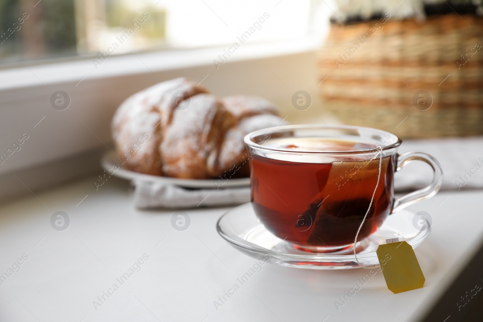 Photo of Tea bag in glass cup on white windowsill. Space for text