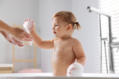 Mother and her baby daughter playing with foam in bathroom