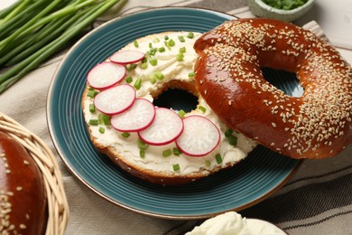 Photo of Delicious bagel with cream cheese, green onion and radish on table, closeup