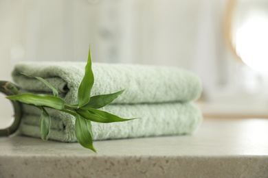 Photo of Stack of clean towels and bamboo sprout on table in bathroom