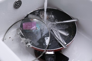 Photo of Pouring water on dirty kitchenware and cutlery in sink