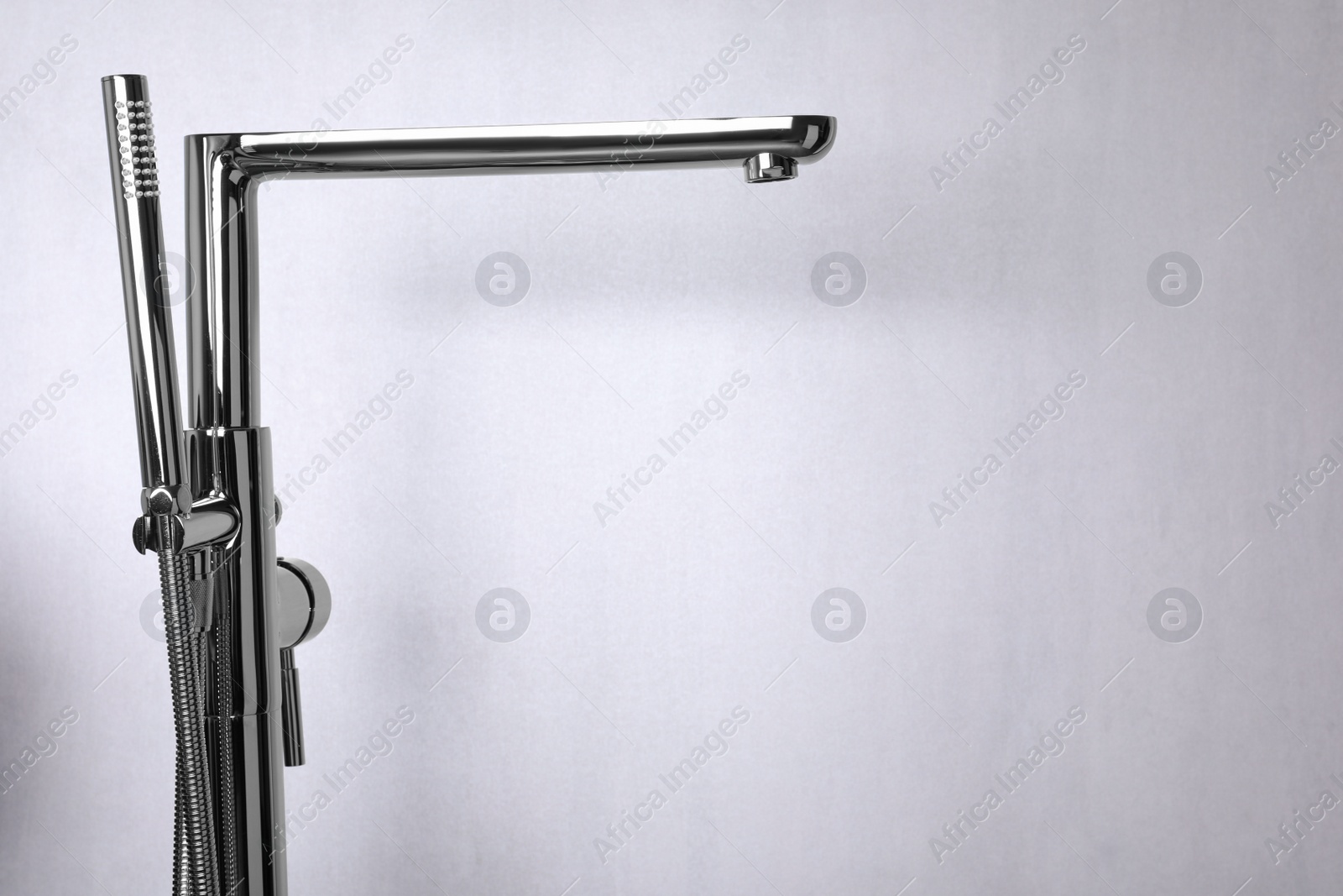 Photo of Modern bathtub faucet with hand shower on light grey background. Space for text