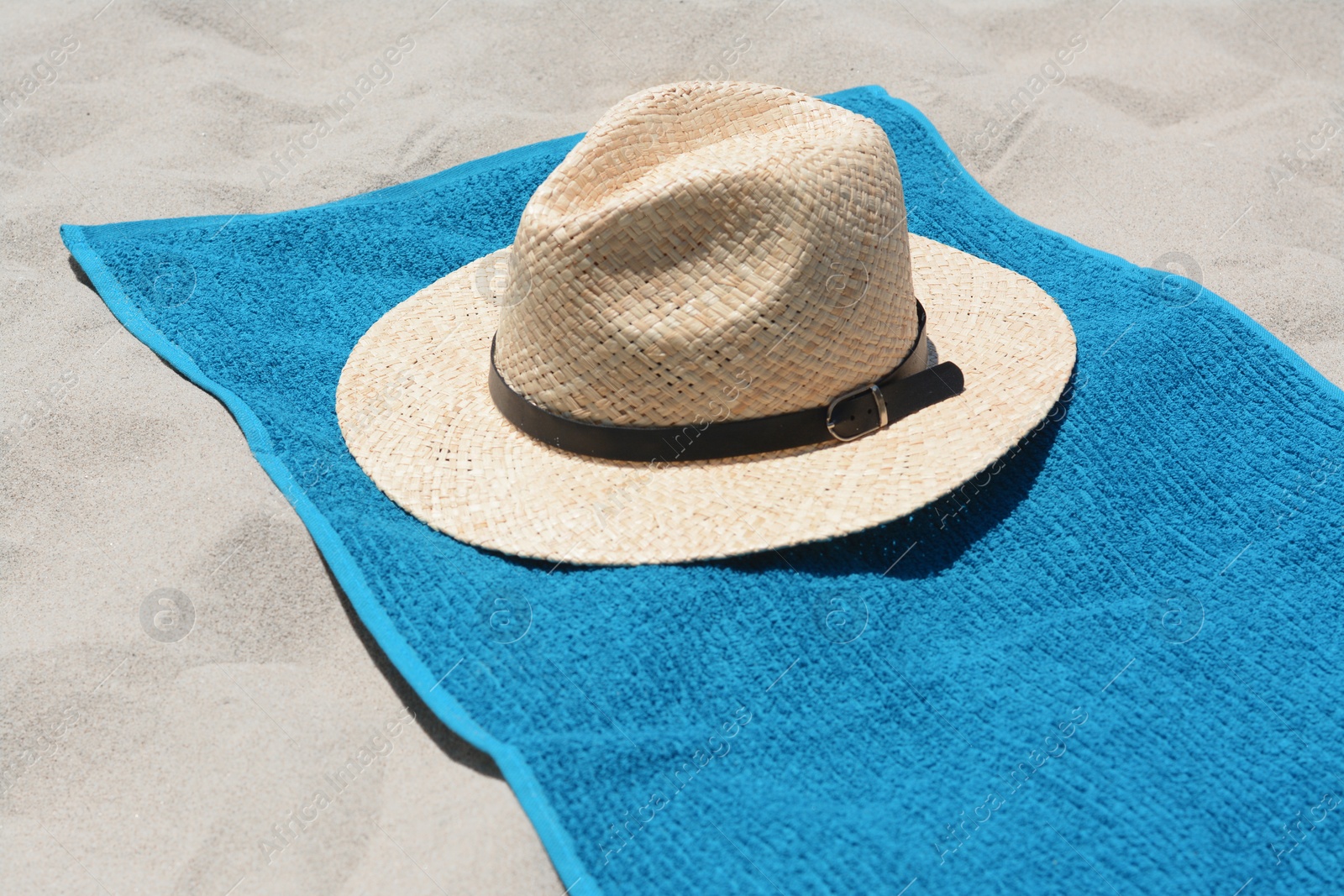Photo of Soft blue towel and straw hat on sandy beach
