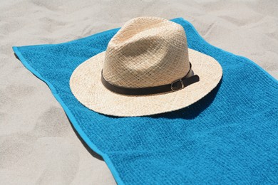 Photo of Soft blue towel and straw hat on sandy beach