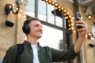 Photo of Smiling man in headphones taking selfie outdoors, low angle view