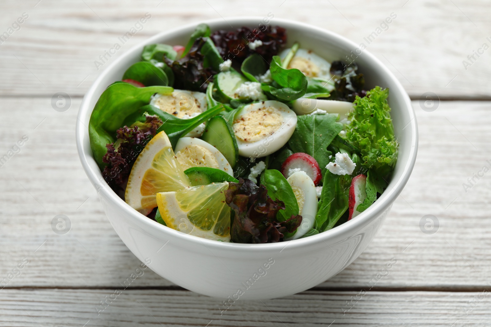 Photo of Delicious salad with boiled eggs, vegetables and lemon in bowl on white wooden table, closeup