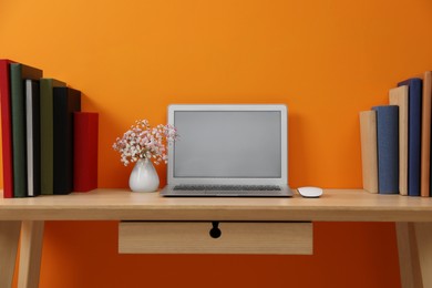 Hardcover books and laptop on wooden table near orange wall