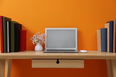 Photo of Hardcover books and laptop on wooden table near orange wall