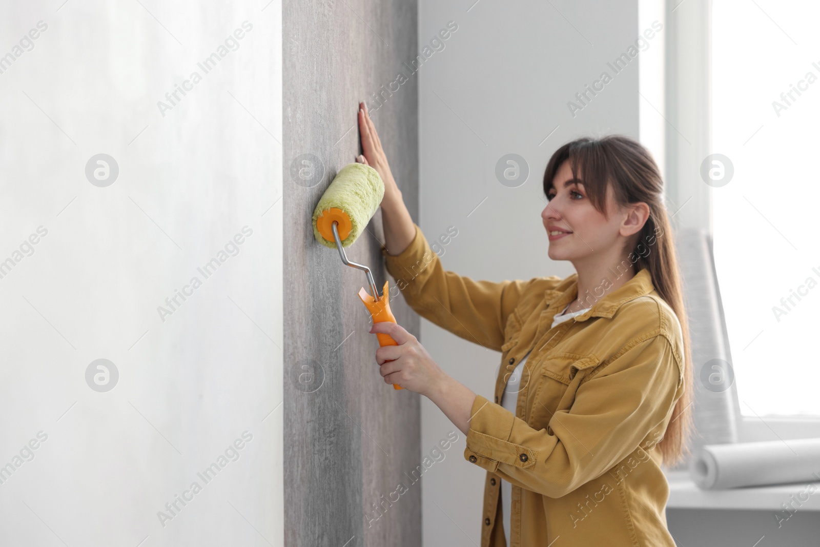 Photo of Woman hanging stylish gray wallpaper in room