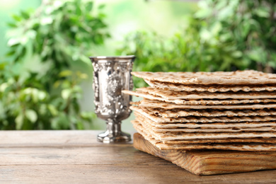 Photo of Traditional Matzos and silver goblet on wooden table, space for text. Pesach (Passover) celebration