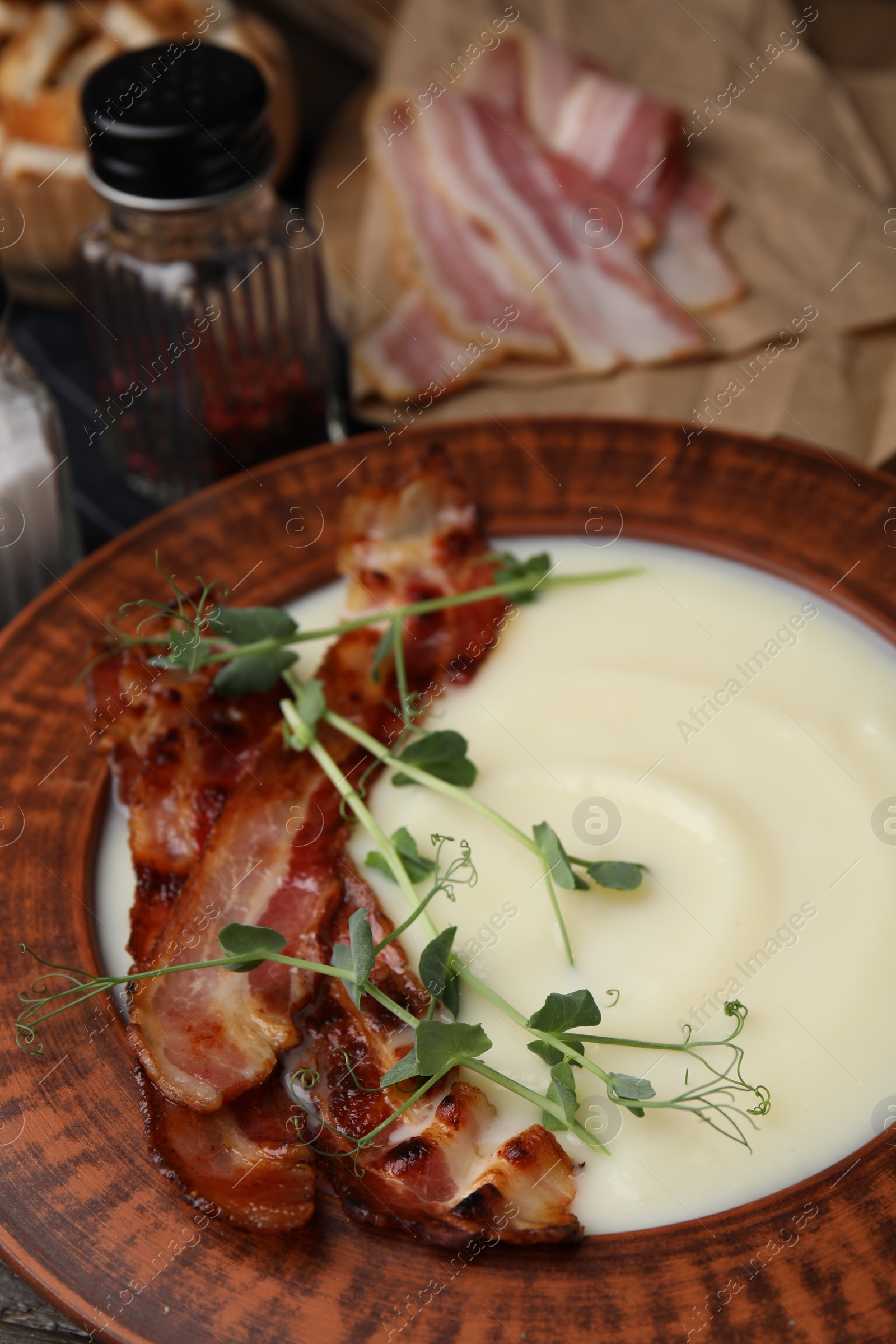 Photo of Delicious potato soup with bacon and microgreens in bowl on table, closeup