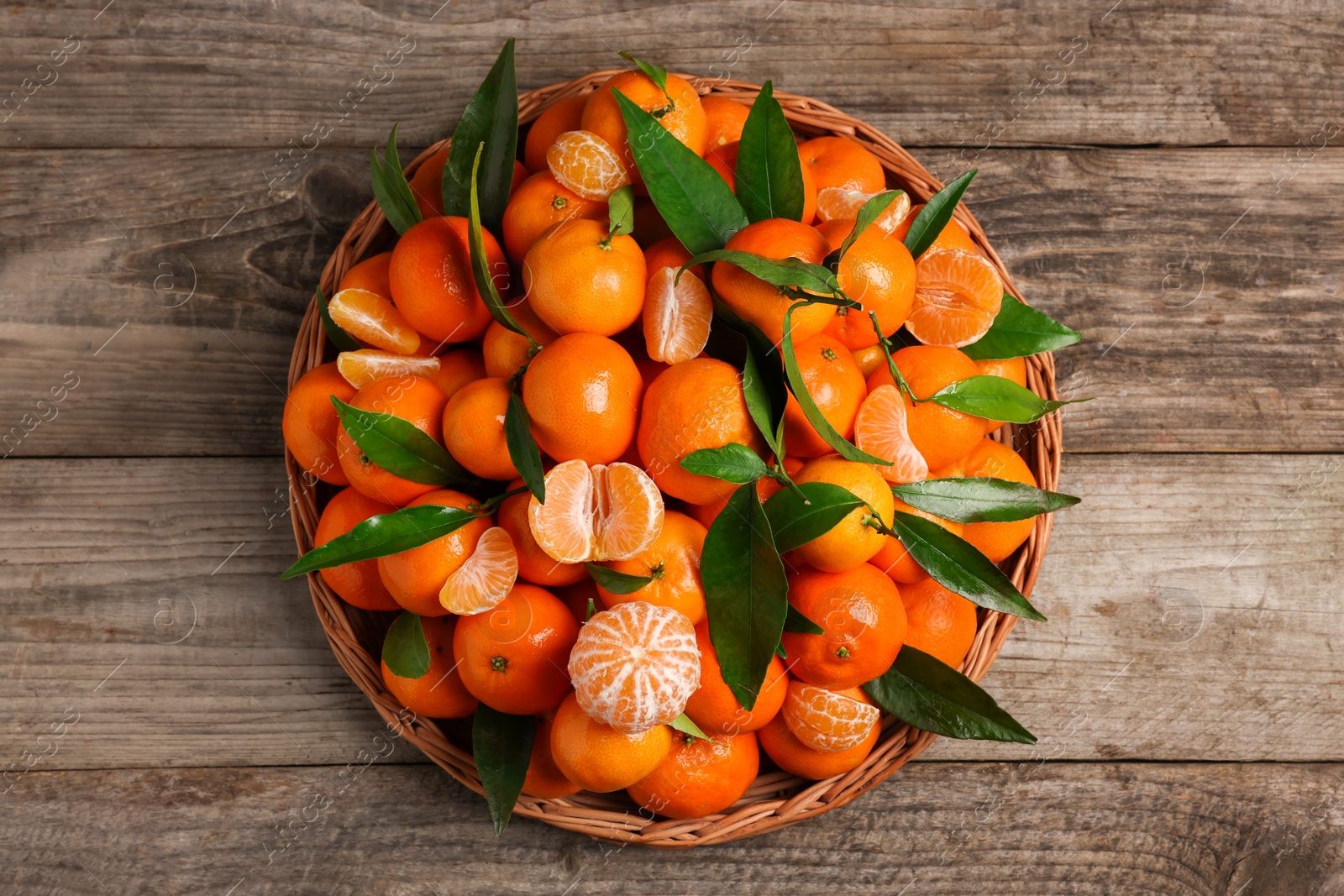 Photo of Fresh ripe juicy tangerines and green leaves on wooden table, top view