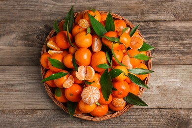 Photo of Fresh ripe juicy tangerines and green leaves on wooden table, top view