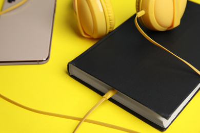 Photo of Book, modern headphones and smartphone on yellow background, closeup