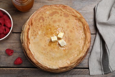 Stack of delicious crepes served with butter, honey and raspberries on wooden table, flat lay