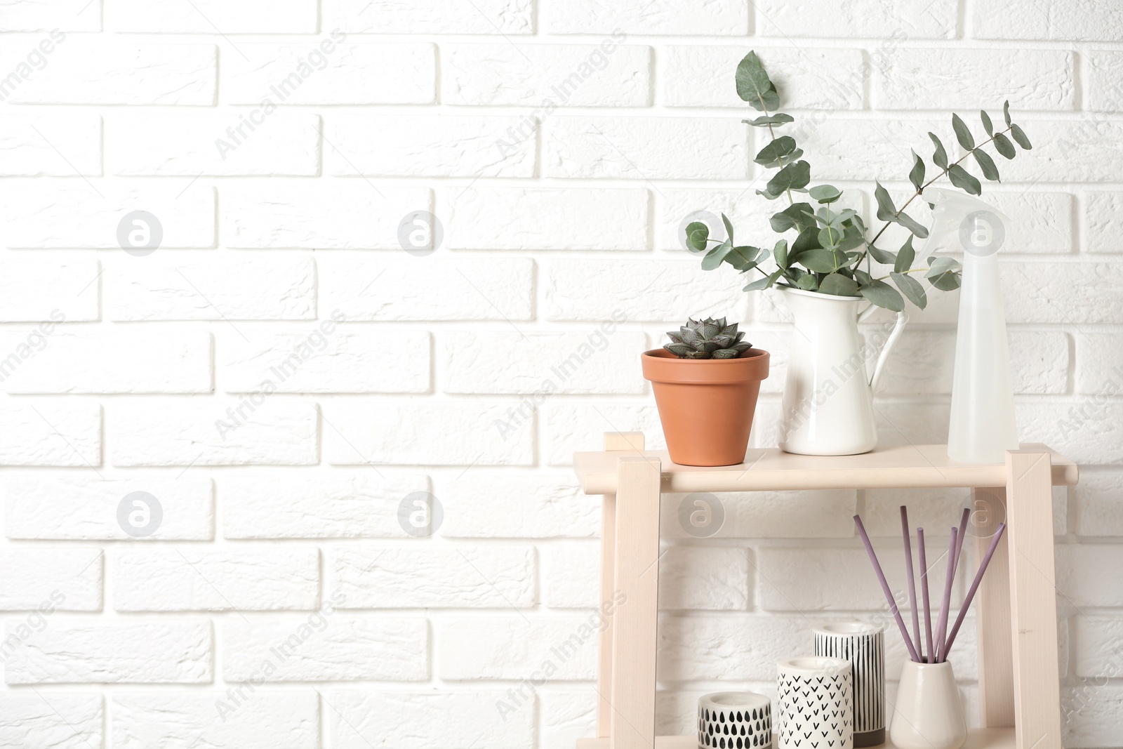 Photo of Beautiful plants and accessories on wooden shelves near brick wall at home. Space for text