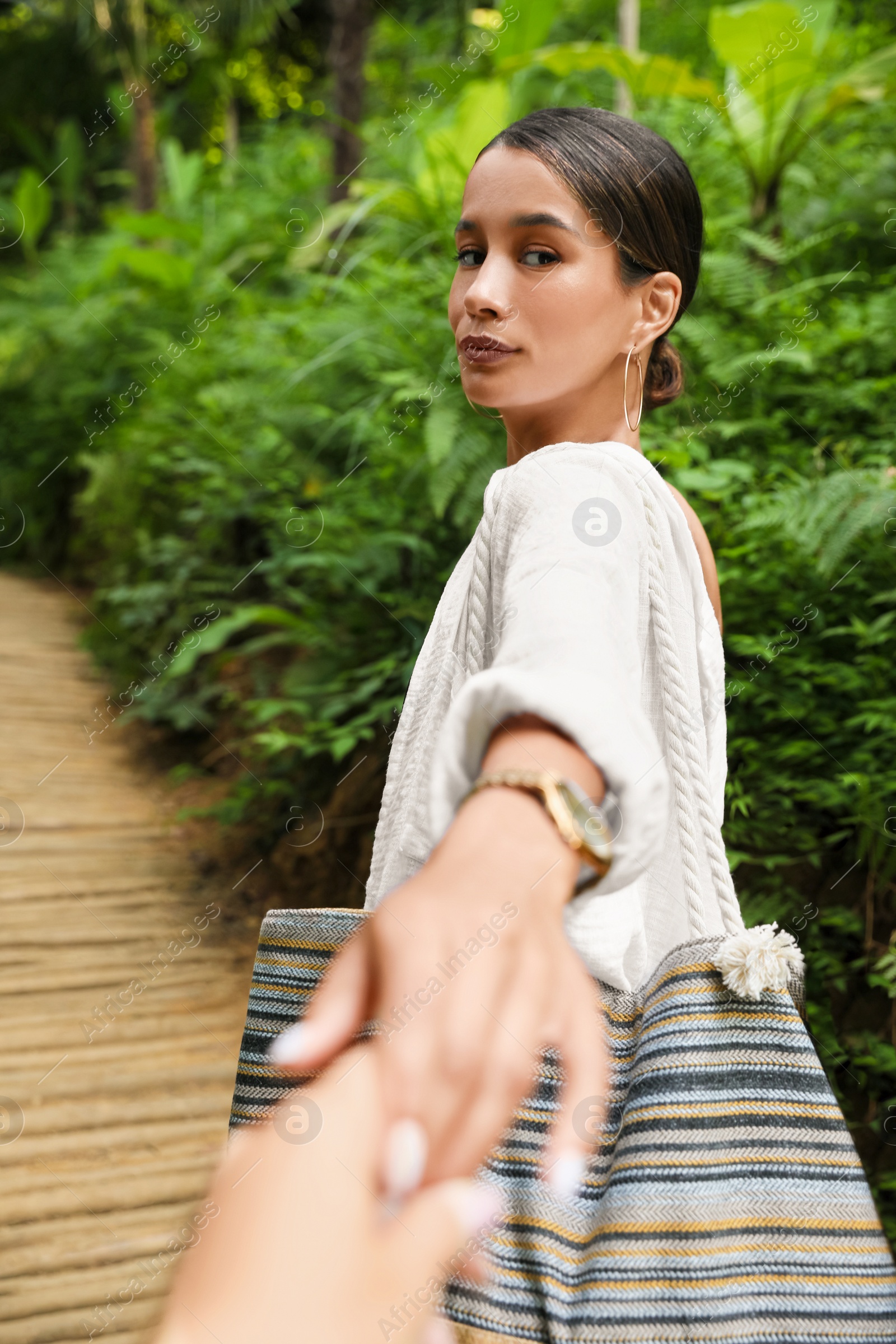 Photo of Young woman holding boyfriend's hand in green tropical park