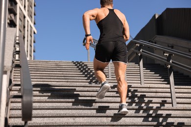 Photo of Man running up stairs outdoors on sunny day, back view