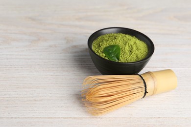 Green matcha powder and bamboo whisk on white wooden table, closeup. Space for text