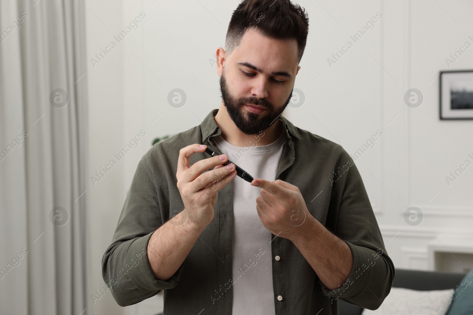 Photo of Diabetes test. Man checking blood sugar level with lancet pen at home