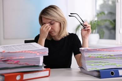 Photo of Overwhelmed woman sitting at table with stacks of documents and folders in office