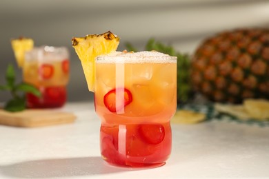 Spicy pineapple cocktail with chili pepper and ice cubes on white table, closeup