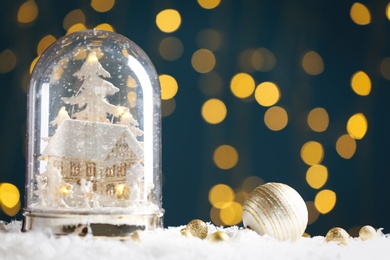 Photo of Beautiful snow globe and baubles against blurred Christmas lights. Space for text