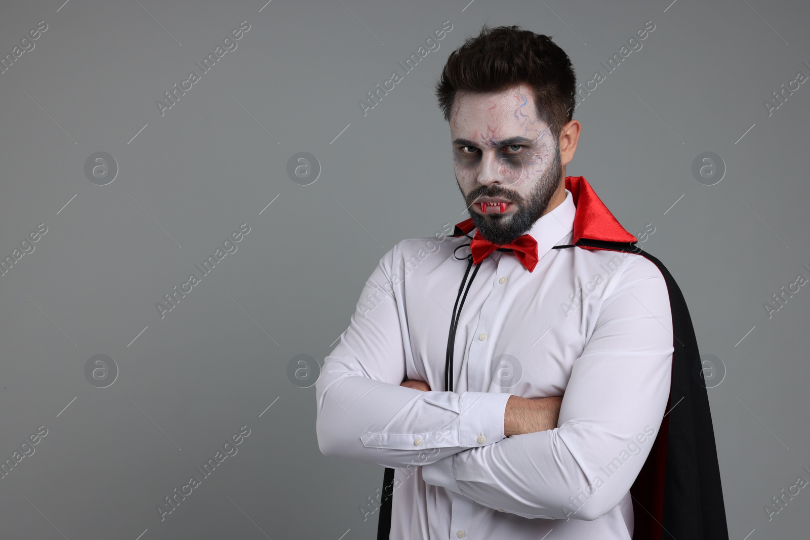 Photo of Man in scary vampire costume with fangs on light grey background, space for text. Halloween celebration