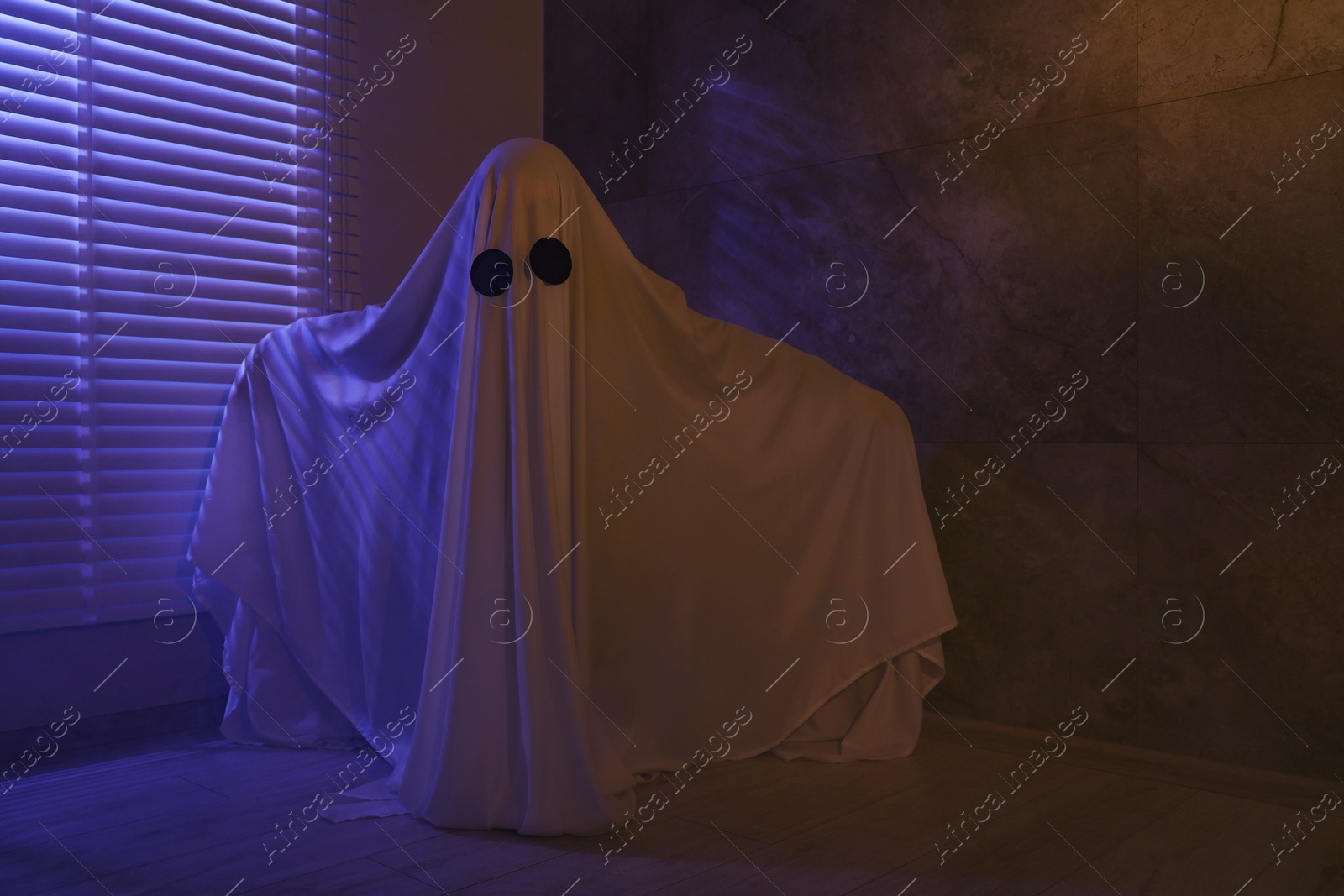 Photo of Creepy ghost. Woman covered with sheet near window in color lights