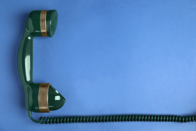 Photo of Handset of vintage green telephone on blue background, top view. Space for text