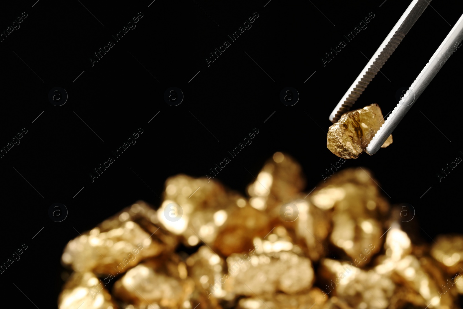 Photo of Tweezers with gold nugget against blurred background, closeup. Space for text