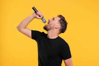 Handsome man with microphone singing on yellow background