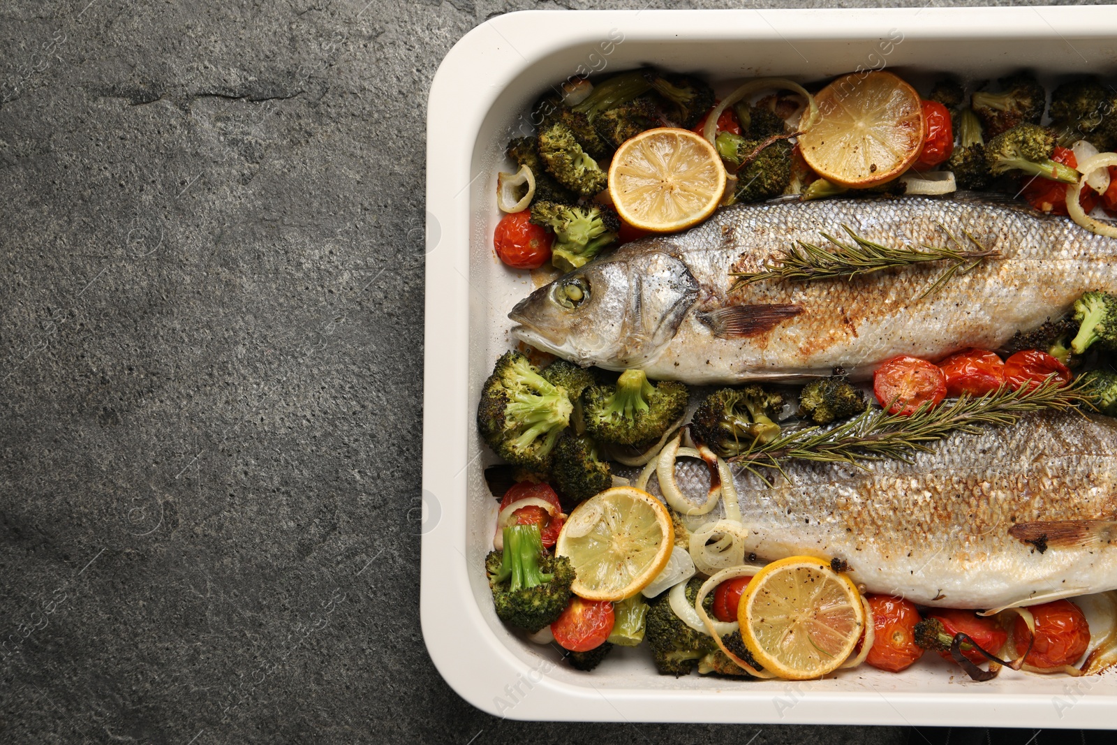 Photo of Delicious fish with vegetables and lemon in baking dish on grey textured table, top view. Space for text