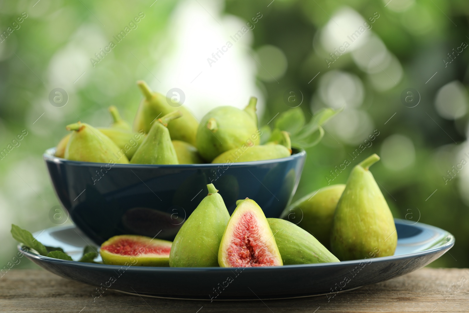 Photo of Cut and whole green figs on wooden table against blurred background, closeup
