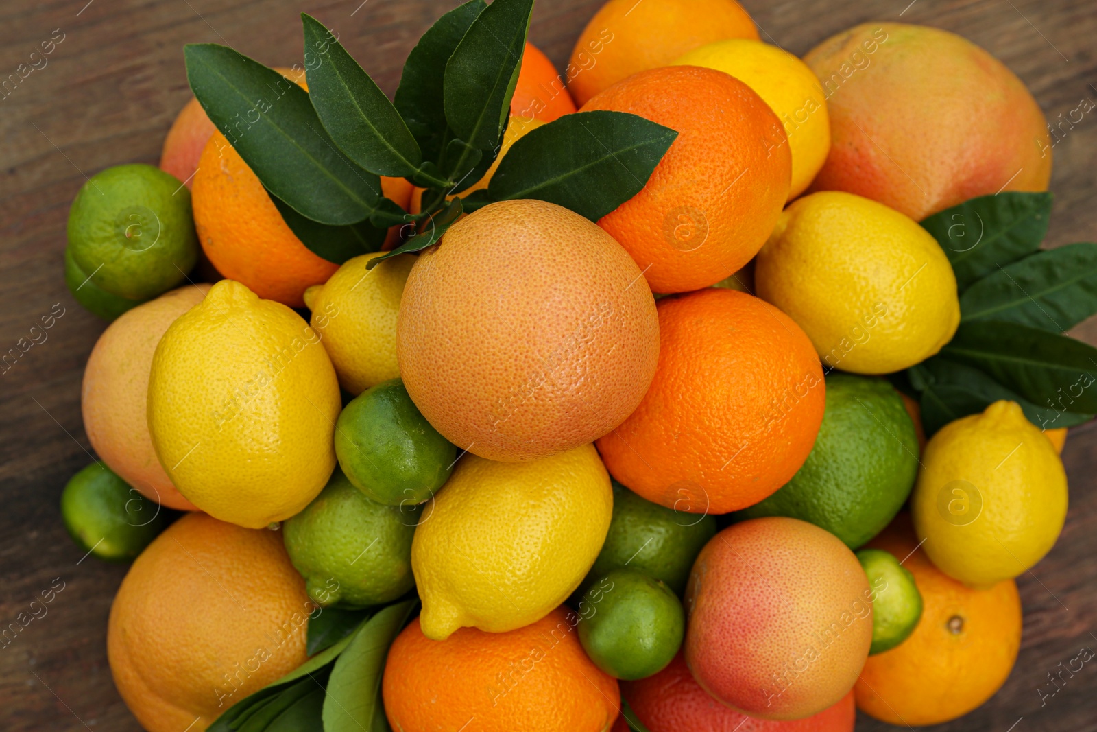 Photo of Different citrus fruits and leaves on wooden table, closeup