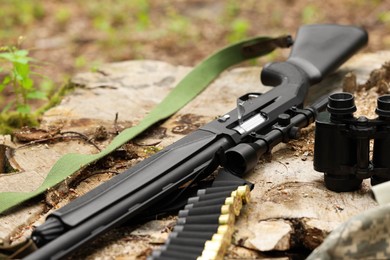 Photo of Hunting rifle, cartridges and binoculars on tree stump outdoors, closeup