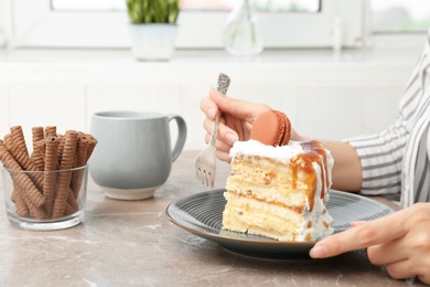 Photo of Woman eating delicious homemade cake with caramel sauce at table